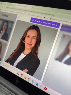 A young woman with long brown hair and green eyes is looking at the camera with a smile while on a laptop.