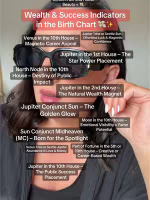 A woman wearing sunglasses is holding up a visual aid, likely a chart which displays a list of astrological indications for wealth and success in a birth chart. The image uses a soft, professional aesthetic with a focus on the presenter wearing a black top, black frame sunglasses, and pink lipstick. The background is blurred, keeping the focus on the topic and the presenter. Text is overlaid to further relay ideas, in white font with a red banner color. The lighting accentuates the presenter's features.