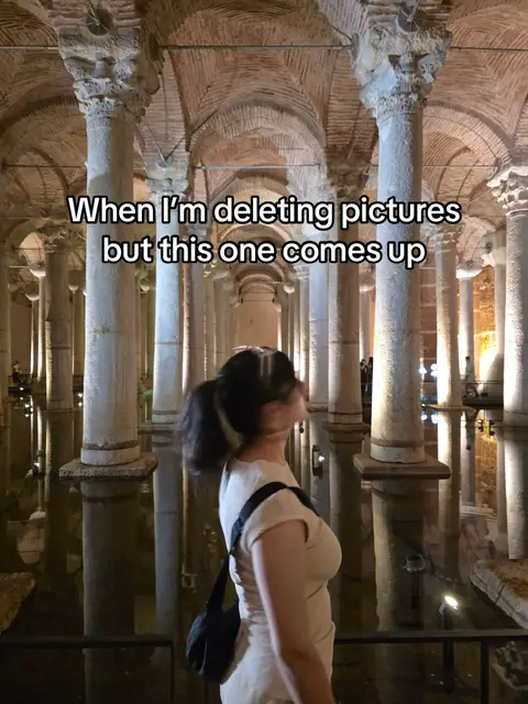 A woman stands in a large, ancient-looking underground space with stone pillars and water. The text overlay reads "When I'm deleting pictures but this one comes up."