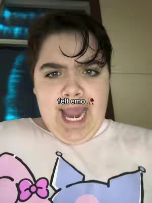 A close-up shot of a person with a focused expression, wearing a light-colored t-shirt with colorful cartoon characters at the bottom. The person has short, dark hair and is looking directly at the camera with a slightly open mouth. The text overlay on the image reads felt emo with a rose emoji.