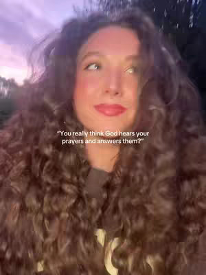 The cover image features a young woman with long, curly brown hair framing her face. She's looking slightly upwards with a thoughtful expression, her eyes and lips are highlighted with makeup. She is set against a blurred background of lavender and soft pink colors from the sunset.