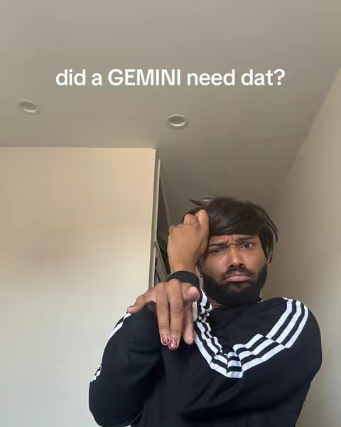 A man with dark hair and a light skin tone is the primary subject, positioned in the foreground. He wears a black Adidas track jacket with white stripes on the sleeves. He has a short beard, and is interacting with the camera with an expressive, possibly humorous, facial expression. The background is simple, showing light-colored walls and a visible ceiling. The composition is a medium shot that focuses on the man's upper body and face; in the background, there is some visibility of the room interior. The aesthetic is casual and modern.
