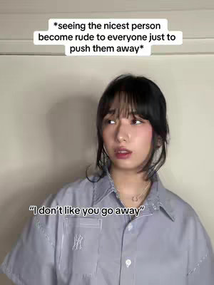 A young woman with dark hair and bangs looking to the side with a serious expression. She is wearing a light blue button-down shirt. Above her is a text overlay in a white rectangle.