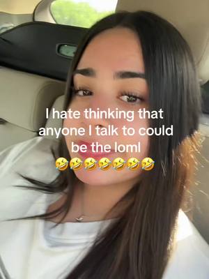 A selfie-style video cover image featuring a young woman inside a vehicle. The woman, with long dark hair, is positioned in the center of the frame with her head and shoulders visible. She has a slightly smiling expression, with visible eyes and a portion of her mouth. Text is overlaid at the top, centered, in white font: "I hate thinking that anyone I talk to could be the loml". Underneath the text, there are seven emojis. The background includes the interior of the car, with a black headrest visible and hints of the outside through the windows. The overall composition is well-lit, with the primary focus on the woman and the overlaid text.