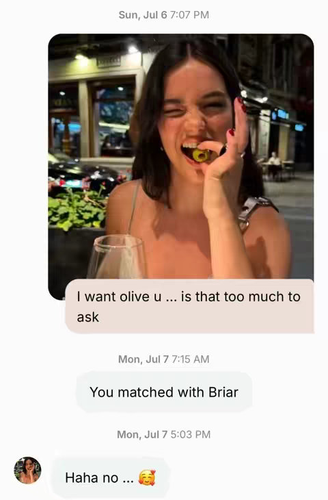 The image shows a young woman indoors, appearing at the top of a text message exchange.  She looks happy and is holding an olive in her mouth, and seems to have red nail polish .  Below, other messages appear, with a message stating 'Haha no ...' and an emoji of a smiling face with hearts for eyes.