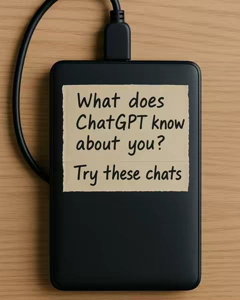 A top-down shot of a black external hard drive sitting on a wooden surface, with a black USB cable plugged into it. A piece of tan-colored paper, resembling a sticky note, is adhered to the hard drive. The paper has handwritten text in a black, simple font, reading "What does ChatGPT know about you?" followed by "Try these chats". The background is a light brown, wooden surface.