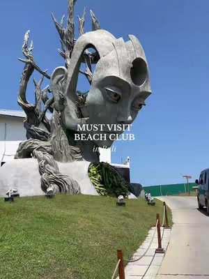The cover image showcases a large, abstract sculpture of a human face, possibly female due to the delicate features and implied long hair flowing to the side. The sculpture is made of a light gray stone and is set against a backdrop of a vibrant blue sky. The sculpture is set on a grassy area with a pathway.
