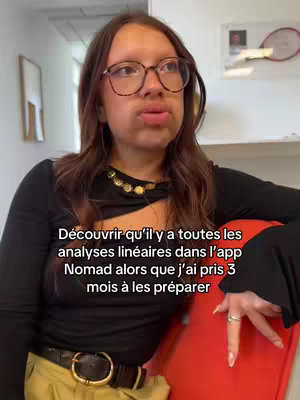 A woman with glasses looks quizzically at the camera. The text overlay on image reads 'Découvrir qu'il y a toutes les analyses linéaires dans l'app Nomad alors que j'ai pris 3 mois à les préparer'. The woman is wearing a black top with gold chain and sitting near a red chair.