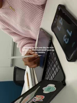 The image shows a person's arm and hand, wearing a pink sweater, resting on a white surface. They are holding a stylus over a tablet, with a laptop and phone visible in the background. Text overlays the image.