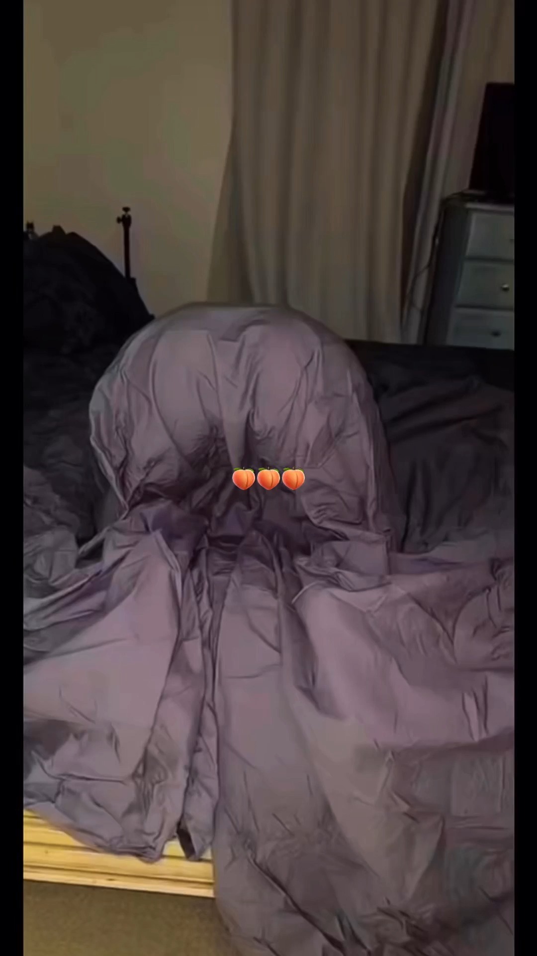 The cover image shows a person lying in bed covered by a purple comforter. Three peach emojis are superimposed on the comforter. The background includes a bedside table, a lamp, and curtains.