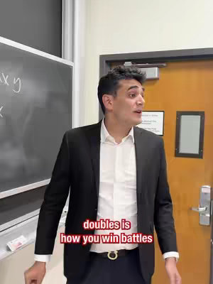 A man in a suit stands in a classroom setting, speaking. The background includes a chalkboard with writing and a door. Text overlayed at the bottom of the image reads 'doubles is how you win battles'.