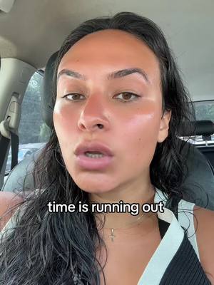 Close-up shot of a woman inside of a car. She has dark hair and is looking directly at the camera with a slightly open mouth, as if speaking. Overlayed on the image is the text 'time is running out'.