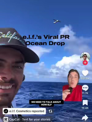 The cover image is a vertical video frame with a split layout. On the left, a man with a beard and a baseball cap is shown from the chest up, partially obscuring the frame with his face. His eyes are looking left with a slight smile. Behind him, the ocean stretches to the horizon under a blue sky with some clouds and the sun. An airplane is flying in the sky. On the right, there is a smaller inset video featuring a man in a red shirt holding a small black object and speaking with a surprised expression. Overlay text includes the title 'e.l.f.'s Viral PR Ocean Drop'. Additional text at the bottom of the screen mentions 'We need to talk about how elf.' with e.l.f cosmetics reposted and also a 'CapCut - Text for your stories'.