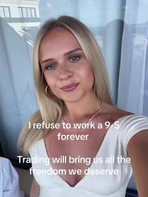 A woman with long blonde hair poses in front of a window, wearing a white top and a gold necklace and earrings. Text overlays read, 'I refuse to work a 9-5 forever' and 'Trading will bring us all the freedom we deserve'.