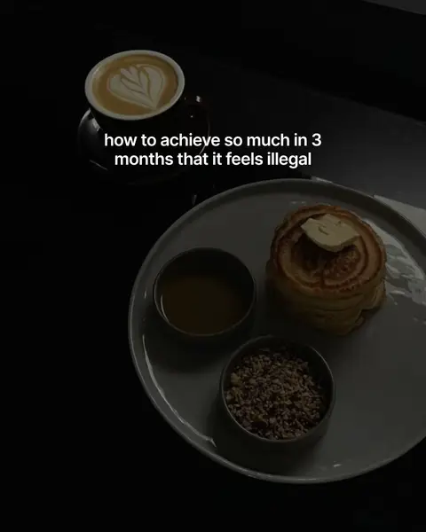 A still-life image featuring a dark, moody aesthetic. A cup of coffee with latte art sits on a black saucer at the top. Below, a gray plate holds pancakes with a pat of butter, accompanied by small bowls of honey and granola. The background shadow enhances the arrangement.