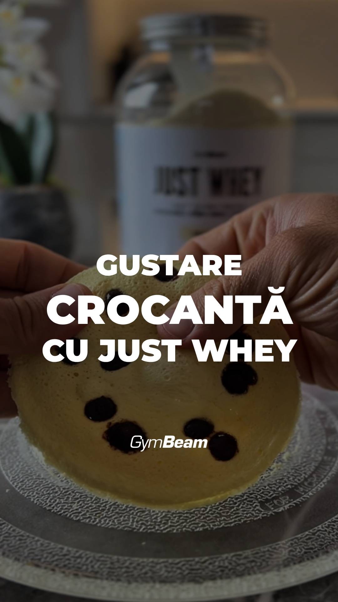 The image shows a person's hands holding a partially eaten pancake with dark chocolate chips on a clear glass plate. In the background, a blurred container of a product labeled "Just Whey" is visible. Bold white text overlays say "GUSTARE CROCANTĂ CU JUST WHEY". The logo of the brand "GymBeam" is in the bottom left corner.