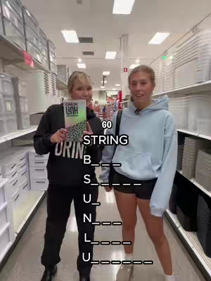 Two women stand in a retail store aisle. One holds a book with a cover that has the words "CHAIN LINK" on it. The other is wearing light blue hoodie. Text is overlaid, showing a word puzzle for "STRING".