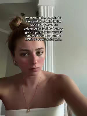 A selfie-style image featuring a young woman centered in the frame. She has fair skin, is wearing a strapless white top, and her hair is pulled up in a bun. Text overlays are present at the top, displayed in a white font. The background is blurred, but appears to be indoors with indistinct details, indicating the shot likely taken at home.
