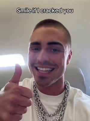 The cover image is a selfie featuring a smiling man giving a thumbs-up. The man, with short, dark hair and eyebrows, is wearing a white t-shirt and multiple silver chain necklaces. The background suggests a light environment, as if indoors, and there is text overlayed at the top.