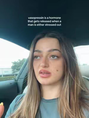 A woman with long, light brown hair is seated in a car. She has a slightly distressed expression, with her upper lip slightly raised. Text overlayed on the image reads: "vasopressin is a hormone that gets released when a man is either stressed out". The interior of the car and some of the exterior environment are visible as a backdrop.