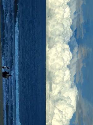 The image is split vertically, showing the left side as a dark blue sea scene with small silhouettes of people on the shore, and the right side filled with fluffy white clouds against a light blue sky. The composition is divided evenly, showcasing a contrast between the ocean and sky.