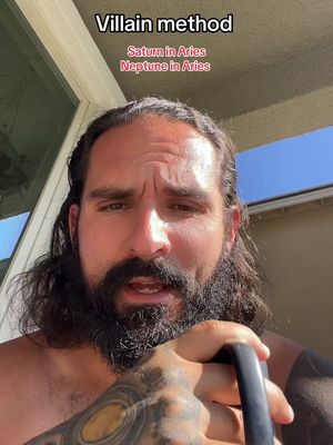 A man with a beard and long hair is positioned in front of a window, with text overlays at the top. The man, with a serious expression, is holding an object, possibly a kettlebell, in his right hand. The background includes an outdoor setting with sunlight.