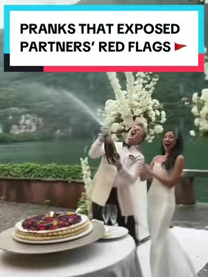 The image captures a wedding scene outdoors with a lush, green background. A man in a white suit is popping a champagne bottle, with the spray of champagne in the air. A woman in a white gown stands beside him, looking surprised and reacting with a joyous expression. Behind them, a large floral arrangement adds to the celebratory atmosphere. In the foreground, a cake is decorated with berries.
