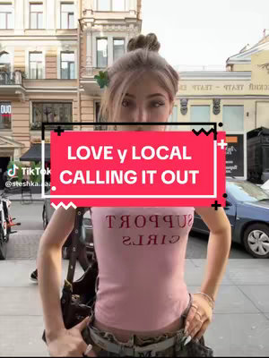 A young woman with light hair stands on a city street, wearing a pink tank top, and looking towards the camera. The background features buildings and a blue car, with the primary focus on the text overlay in a red rectangle: "LOVE y LOCAL CALLING IT OUT."