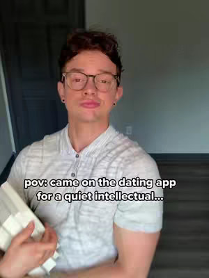 A man with glasses and a light-colored shirt holds a stack of books, standing in a room with a dark door and plain wall, with the overlay text "pov: came on the dating app for a quiet intellectual…"