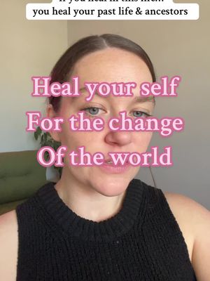 A selfie-style portrait featuring a woman with fair skin and light brown hair. She's wearing a black top and positioned in front of a soft, slightly out-of-focus background, possibly a light-colored wall with a glimpse of a green object on the left. The primary colors are neutral with highlights from the text. The main focus is on her face, where overlaid text in a pink hue is placed.