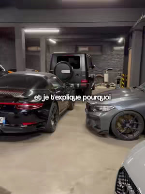 A shot of a garage with several luxury cars, including a black Porsche on the left, a gray BMW M car in the center, and a black Mercedes and a black SUV in the background. The text overlay reads: “et je t’explique pourquoi”. The garage is well-lit with fluorescent lights, and the setting is industrial.