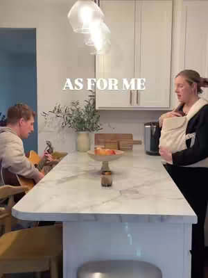 A man playing a guitar and a woman holding a baby in a kitchen setting, text overlayed.