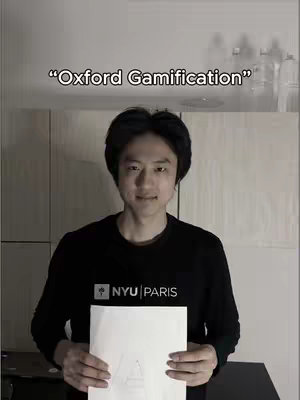 A man wearing a black sweater with the NYU Paris logo holds a blank white paper. Above him is text that says "Oxford Gamification". The background is a simple white wall.