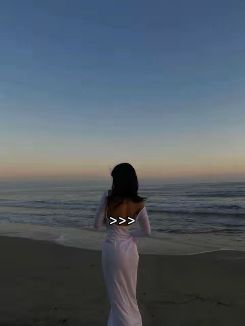 A woman stands on a beach at sunset, facing away from the camera. She wears a long white dress, and the text overlay is in a light color. The background shows the sea under a colorful sky. The image's composition is aesthetically pleasing, giving a sense of calm and freedom.