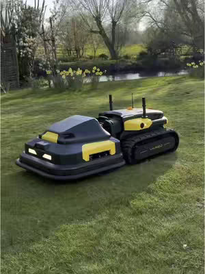 The image shows a robot lawnmower set against a backdrop of a lush, green lawn, trees, and a body of water. The lawnmower is comprised of two connected parts: a boxy, covered section with a black base and yellow trim, and a tracked, yellow and black section. The composition is a medium shot, presenting the lawnmower in detail with a slightly elevated perspective, enhancing the scene's outdoor/tech ambiance.