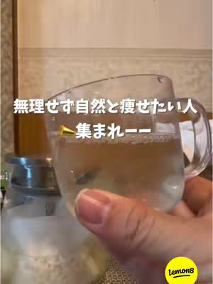 The image shows a clear glass mug filled with a light-colored liquid, likely a drink, in a brightly lit setting. The mug is held by a hand with a well-manicured nail. Text overlays, in a clean, modern font, are present on the image.