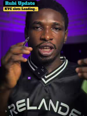 A man with dark skin is the focus of a video cover image. He holds what appears to be a pen or stylus in one hand as he speaks, the other hand is out of frame. He is wearing an athletic jersey with text that says “IRELAND” on it. A microphone is clipped to his neckline, and text overlays at the top says “ Rubi Update” and “KYC slots Loading…”. The background appears to be a gradient of purple.