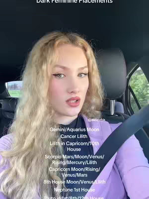 A woman with long, wavy blonde hair looks towards the camera with a slightly open mouth, set against the interior of a car. Text overlays inform the viewer about specific astrological placements.