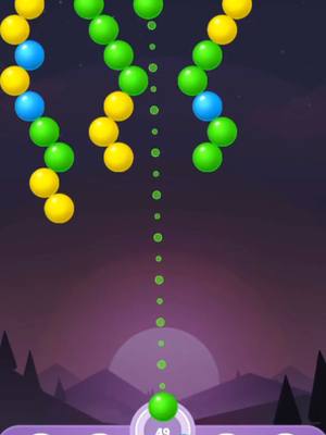 The image shows a screenshot of a mobile game. Colored bubbles are falling from the top of the screen. At the bottom, there's a platform with a bubble ready to be launched. The background has a purple gradient with a silhouette of mountains and a moon.