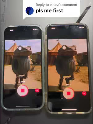 The cover image shows two smartphones displaying the same video on their screens. The video features a green frog-like character with white glowing eyes, walking in front of a circus tent. The background has a warm, yellowish tone. At the top, there is a comment bubble with the text 'pls me first'. Both phone screens are superimposed on a gray background and the frames. One is slightly bigger than the other in the overall image.