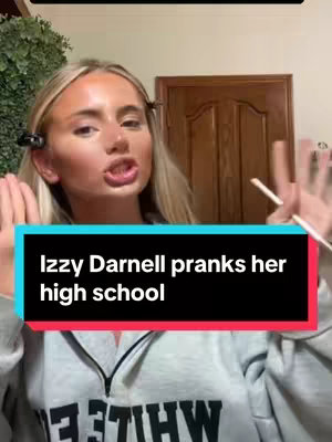 A selfie-style video cover featuring a young woman with blonde hair and makeup, speaking to the camera. She has hair clips on, and her hands are up near her face, with chopsticks in her left hand. Text overlaid on a black bar states "Izzy Darnell pranks her high school."