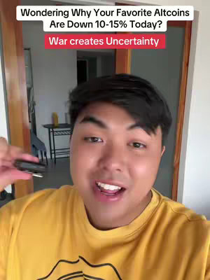 A selfie-style shot with a man in a yellow shirt against an indoor backdrop. The man is centered, smiling and speaking. Overlayed text features at the top with the question: "Wondering Why Your Favorite Altcoins Are Down 10-15% Today?" and a red box right below it containing "War creates Uncertainty". The background is blurred, it seems to be the interior of a building with a doorway and a table.