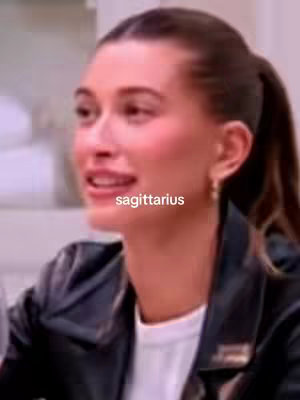 A close-up shot of a person, likely a woman, with their head turned slightly to the side, looking towards the left. They have brown hair pulled back into a ponytail. They wear a black jacket over a white shirt. The text overlay 'sagittarius' appears in a white, sans-serif font near the bottom center of the frame.