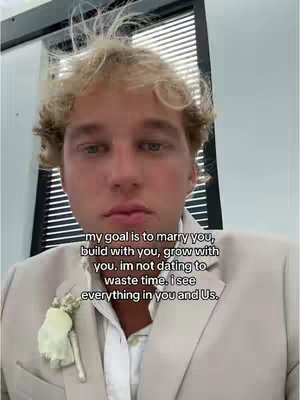 A selfie-style shot featuring a young man with blonde hair and a light-colored suit, the background is slightly blurred and appears to be an interior space. Text is overlaid, expressing a desire for marriage and long-term commitment.