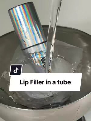 A silver tube-shaped object with a rainbow holographic finish is seen partially submerged in ice water. A clear stream of water is being poured over the object, creating a dynamic visual. The image is set in a stainless steel bowl against a clean white background, and a TikTok logo is present in the bottom left corner.