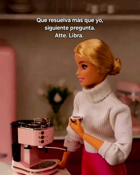 A still image featuring a Barbie doll standing in a kitchen setting. The doll is blonde and wears a white turtleneck sweater and a pink skirt. She holds a small cup with a design in her right hand and is looking to the left. In the background is a pink coffee machine. Text is overlaid at the top, and there is additional text related to the astrological sign Libra.