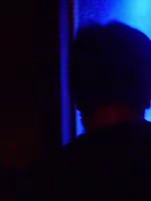 The cover image is dominated by darkness. A person's silhouette is visible, facing away from the viewer and towards a blue-lit area, suggesting a scene in a dimly lit space or near a light source. The overall composition is simple, focusing on the interplay of light and shadow to create an atmosphere.