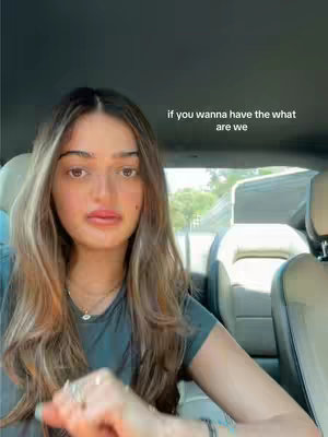 A young woman with long, light brown hair is seated inside a car, facing the camera. She has fair skin, full lips, and appears to be looking directly at the viewer. Text overlayed on the image reads, \"if you wanna have the what are we.\"