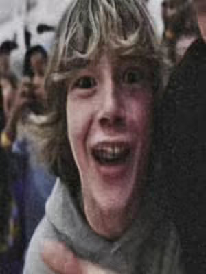 The cover image features a young boy with light brown hair and a gray hoodie, smiling widely with an open mouth. He is surrounded by a crowd of people, some of whom are holding up phones. The image has a slightly grainy quality.