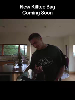 The video cover image shows a man in a dark green Killtec shirt standing in a well-lit kitchen. The man is facing slightly downward, appearing to be observing something in his hands, with a kitchen island and window in the blurred background. The main text is in bold white letters at the top.